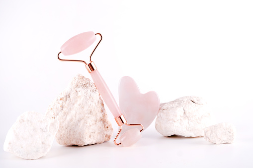 Pink face roller and gua sha massager  quartz  stone over white background.  Lifting and toning treatment at home.