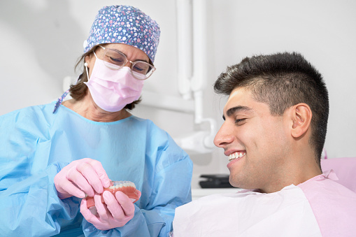 Orthodontist holding invisible retainer for teeth alignment. In clinic shows patient removable transparent plastic aligners or invisalign use and benefit. High quality photo.