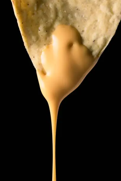 Closeup photo of a nacho with liquid cheese dripping from it on a black background