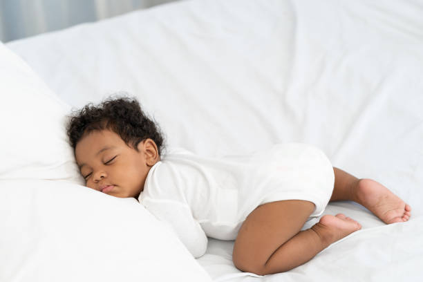 白いマットレスの上で眠っている黒いアフリカ系アメリカ人の赤ちゃん。 - sleeping baby ストックフォトと画像