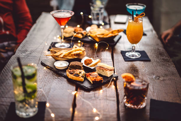 Blurred background of multicolored drinks and minimal food - Happy hour concept with fancy cocktails and tasty appetizers served at rooftop lounge prive - Warm vintage filter on shallow depth of field stock photo