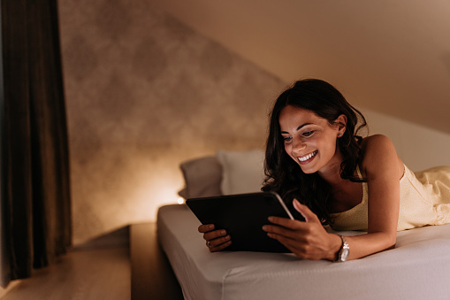 Adult woman, reading a book on her tablet, before sleeping.