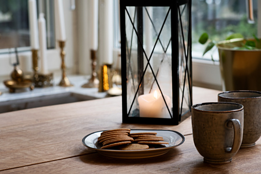 Cosy Christmas holidays morning at home with coffee and gingerbread. Candle light in a lantern, mugs and gingerbread cookies on the wooden table. Photo taken in Sweden.