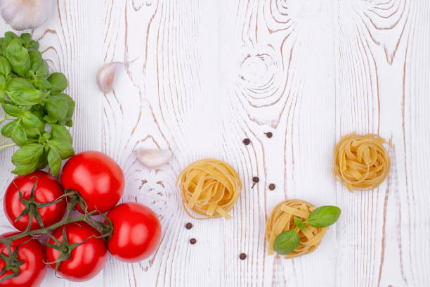 istock Top view raw tagliatelle pasta with fresh basil, garlic and tomatoes on a rustic white table, flat lay, copy space. 1345159419