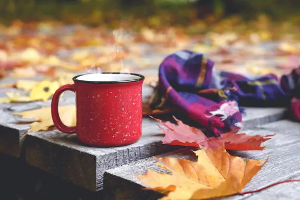 Photo of Autumn coffee or tea in a cup on a wooden table against the background of yellow fallen leaves and October weather. Autumn drink, mood and comfort concept.