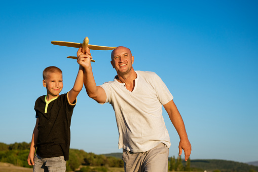 Happy dad and son hold airplane in hand against sky background