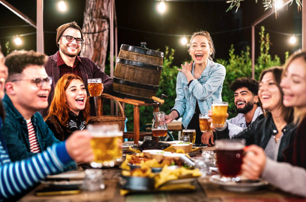 happy men and women having fun drinking out at beer garden - social gathering life style concept on young people enjoying hangout time together at night - warm filter with shallow depth of field - barbecue maaltijd fotos stockfoto's en -beelden