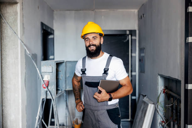 a happy construction worker with a helmet is standing in an unfinished building and holding a tablet under the armpit. he is checking on works on site. - manual worker portrait helmet technology imagens e fotografias de stock