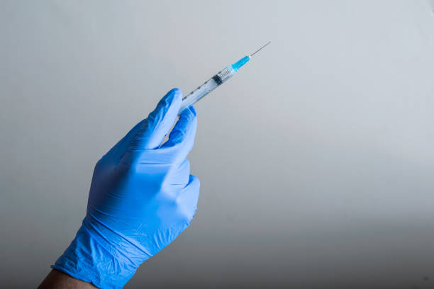 ręka lekarza z niebieskimi gumowymi rękawiczkami, trzymająca strzykawkę gotową do szczepienia, szare zdegradowane tło. narzędzia do szczepień (covid-19, grypa) pandemia i koncepcja zdrowia - copy space left zdjęcia i obrazy z banku zdjęć