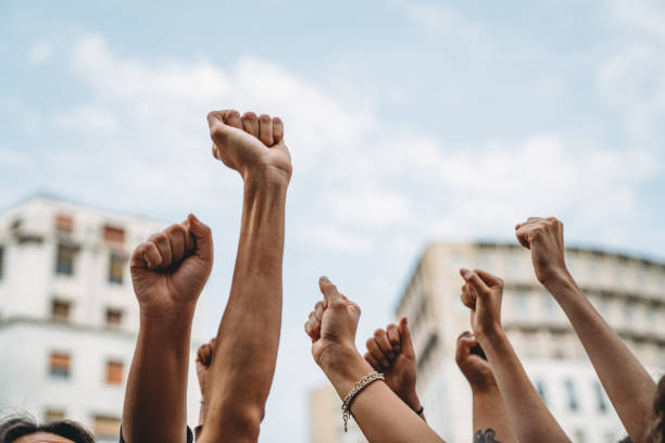 persone con i pugni alzati a una manifestazione in città - diritti umani foto e immagini stock