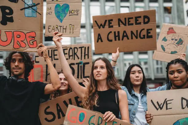 A group of young adult people are marching together on strike against climate change. They are holding cardboard signs. Multi ethnic group of people.