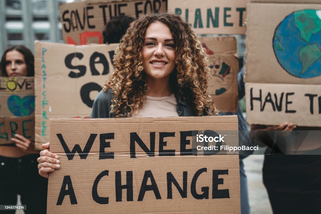 A group of young adult people are marching together on strike against climate change A group of young adult people are marching together on strike against climate change. They are holding cardboard signs. Multi ethnic group of people. Portrait of a girl holding a sign with the text "save our planet" on it. Protest Stock Photo