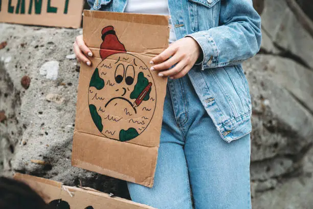 Photo of Detail of a young adult woman holding a cardboard sign with a sick earth drawn on it