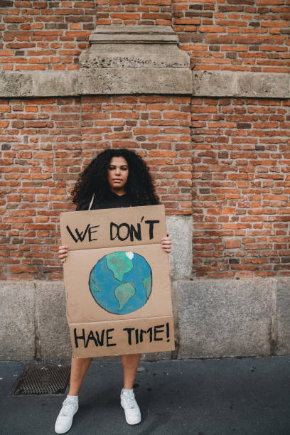 気候変動に反対する段ボールの看板を持つ若い成人女性の肖像画 - global warming city smog heat ストックフォトと画像