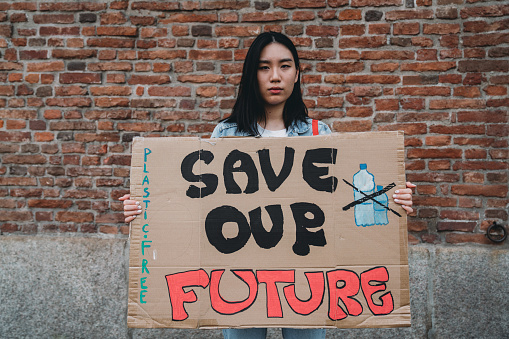 Portrait of a Chinese young adult woman holding a cardboard sign against climate change. The text 