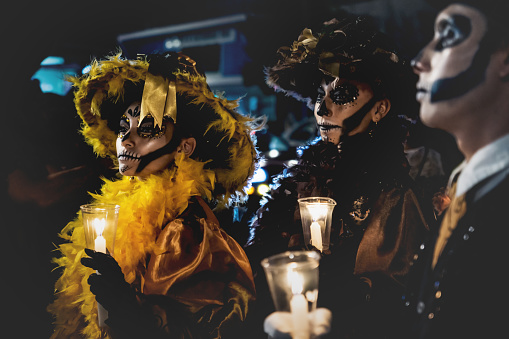 Merida, Mexico: 27 October 2018 - Event for 'dia de los muertos', day of the dead, catrinas with feather costume and skull make up holding candles at the 'Festival de las Animas'