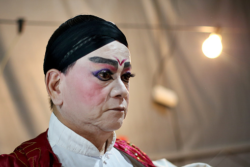 A senior Asian woman is doing her make-up - gearing ready for Chinese Opera performance.