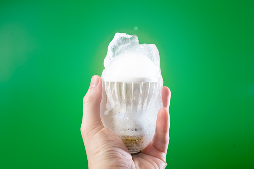 Male hand holding LED lamp frozen in ice on green background