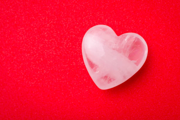 istock White transparent stone in shape of heart on red table 1345179544