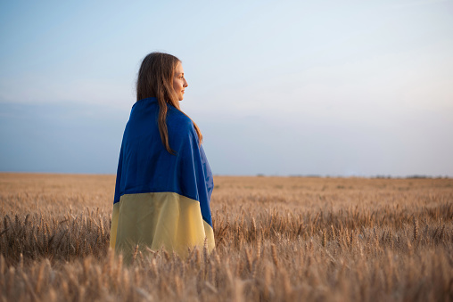 Ukrainian girl with national flag in agricultural field of wheat