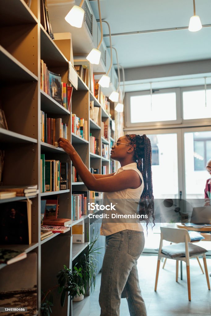 This is my favorite study spot Female student looking at books in the shelf in the library Preparation Stock Photo
