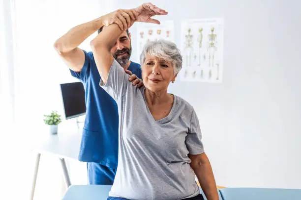 Male doctor chiropractor or osteopath fixing womans shoulder with hands movements during visit in manual therapy clinic