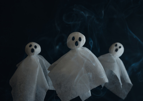 Three white ghosts made from textile napkins on the black background, stock photography for Halloween poster with copy space.