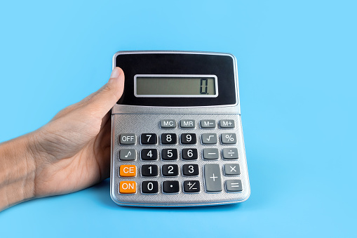 Hand with a calculator on a blue background. The concept of finance, business, money, accounting, savings.