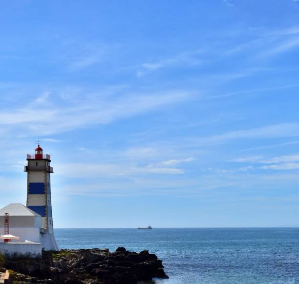 istock Lighthouse tower and ship silhouette on horizon 1345186267