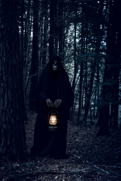 istock Grim Reaper in the dark forest holding a lantern, looking at the camera. 1345187740