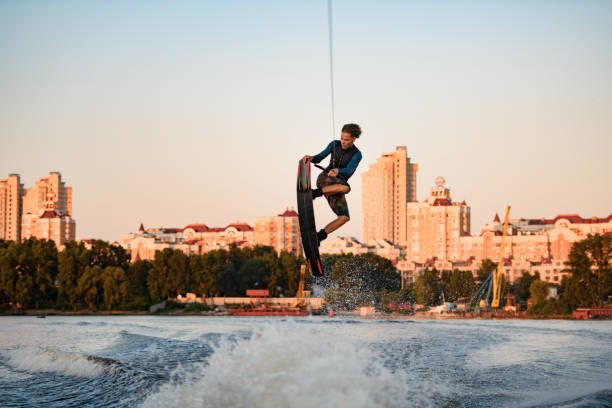 отличный вид здорового активного человека, мастерски прыгающего через плещущиеся волны на вейкборде - wakeboarding waterskiing water ski sunset стоковые фото и изображения