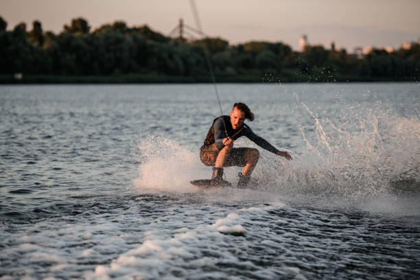 istock energetic man in wetsuit balancing on wakeboard and riding a splashing wave. 1345190223