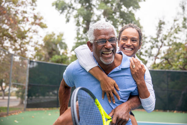 älteres schwarzes paar auf tennisplatz huckepack - tennis active seniors healthy lifestyle senior men stock-fotos und bilder