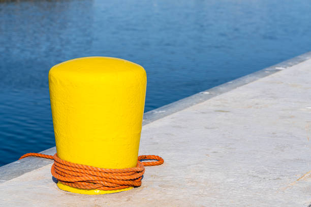 A weathered metal bollard with a rusted surface sits on a concrete pier, secured with a robust chain. The tranquil water backdrop accentuates the maritime atmosphere, blending strength with serenity. Ideal for conceptual visuals representing stability, waterway industry, or vintage coastal charm.