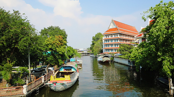 Bangkok canal scene at daytime with moored boats and housing building.