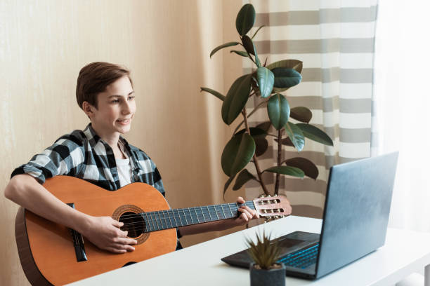 istock Kid boy playing guitar and watching online lessons on laptop while practicing at home. Stay home. quarantine. Online training, online classes 1345197237