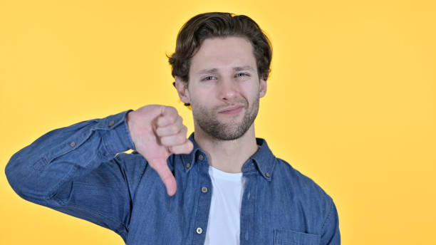 istock Thumbs Down by Disappointed Young Man on Yellow Background 1345197282