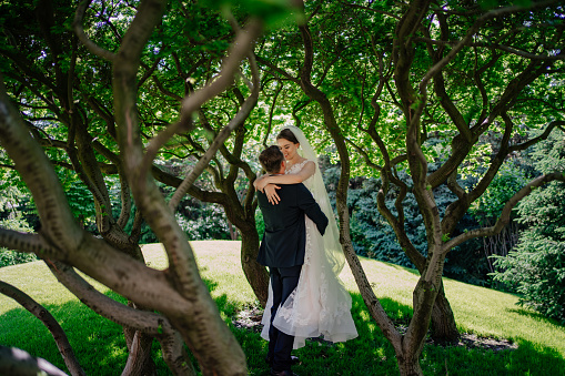 beautiful newlyweds hug by the trees in the park. bride and groom on a walk in nature. tenderness and romance in relationships. wedding planner services. open-air ceremony.