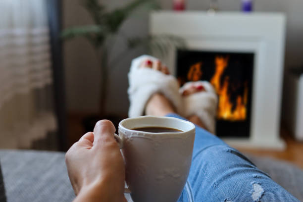 istock Woman drinks coffee and warms legs on fireplace at home 1345197421