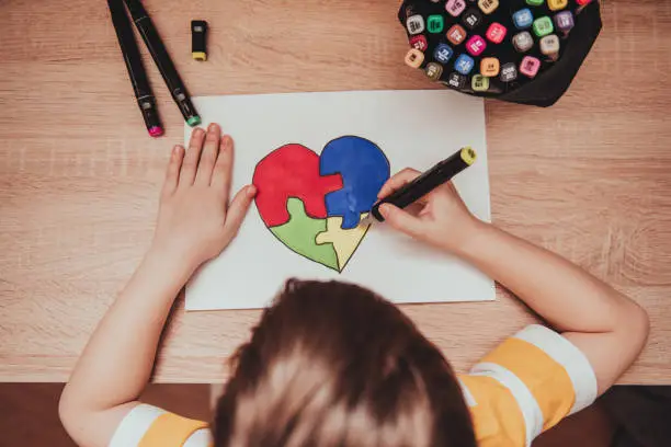 Photo of World Autism Awareness day. Children's hand draws heart from multi-colored puzzles. Mental health care concept