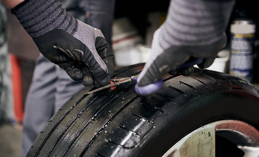 Mechanic Preparing the Nail Hole in a Punctured Tire by Cutting the Injection Moulding before Putting in the Crude Rubber Filler