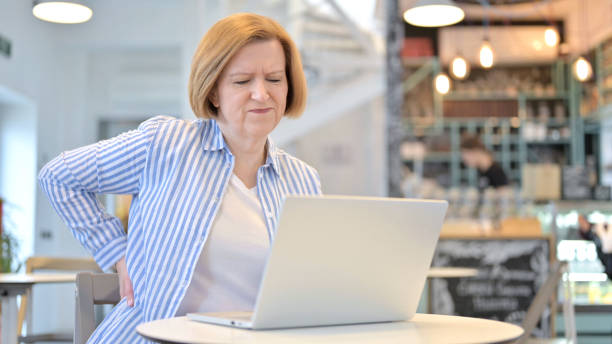 istock Creative Old Woman with Back Pain using Laptop in Cafe 1345201447