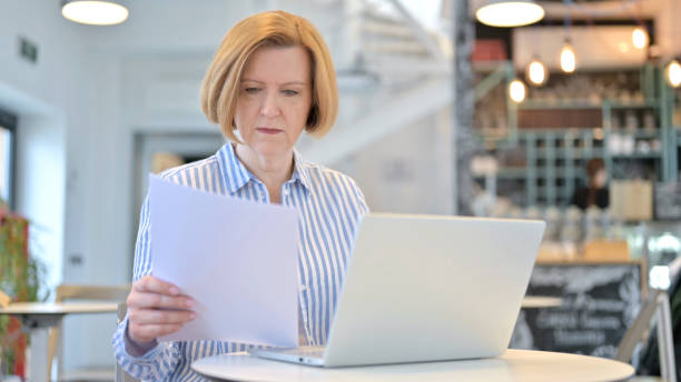 istock Creative Old Woman Working on Laptop and Document in Cafe 1345201581