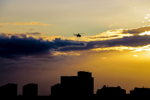 A helicopter flies over the city in the evening during sunset