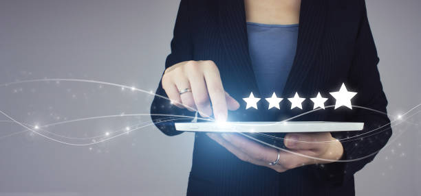 istock Increase rating or ranking, evaluation and classification idea. White tablet in businesswoman hand with digital hologram Five stars 5 rating sign on grey background. Customer Experience Concept. 1345203227