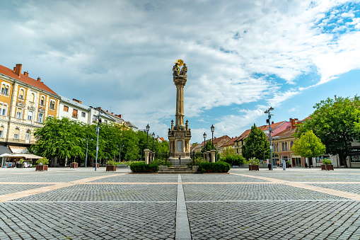 SZOMBATHELY, HUNGARY - AUGUST 15, 2021: View on the Statue of Holy Trinity or the Szentharomsag szobor on the Main square or Fo Square and the people on a sunny, cloudy day in Szombathely, Hungary.