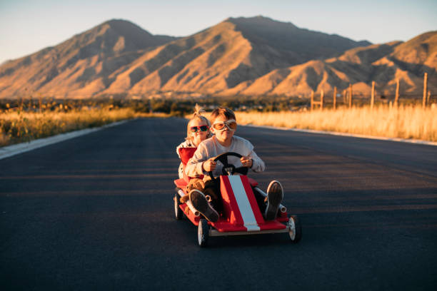 Brother and Sister Go-Cart Racing A brother and sister are racing in their toy go cart and having too much fun. Image taken in Utah, USA. soapbox cart stock pictures, royalty-free photos & images