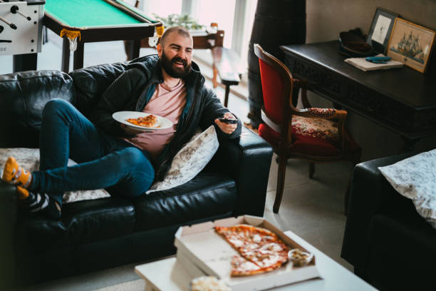 istock Man sitting on a couch eating take-out pizza and watching a TV 1345207289