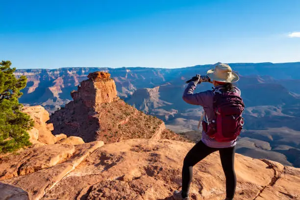 Scenic view of the South Rim of the Grand Canyon. Mature woman on the edge of Canyon  taking a photo with smartphone.