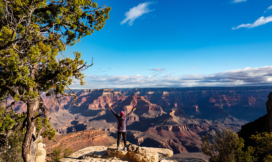 Panoramic Scenic view of the South Rim of the Grand Canyon. Mature woman on the edge of Canyon with arms outstretched.